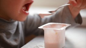 video child eats yogurt with a spoon sitting at the table