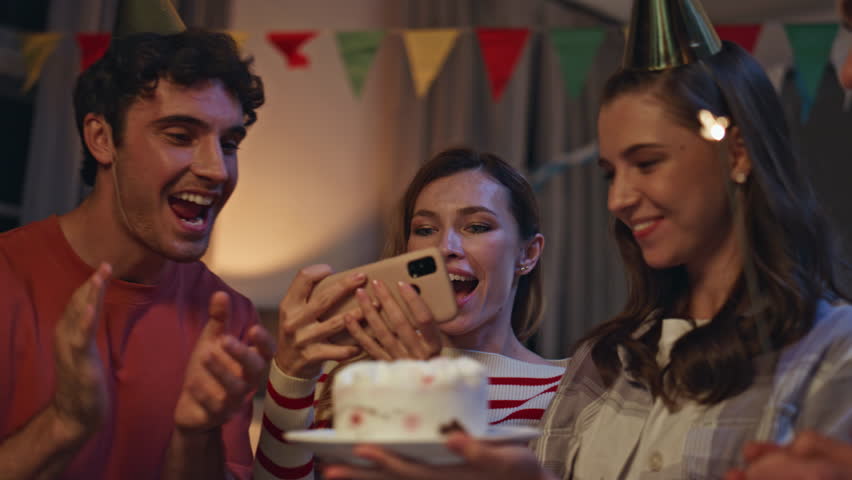 Group taking photo birthday party on smartphone close up. Excited young people making selfie on cell phone holding tasty cake at festive room. Smiling colleagues photographing anniversary celebration.