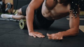 Live camera. Close-up. A multiracial man with dreadlocks on his head does an outer thigh roll with a massage roller while doing a plank position on his elbows in the gym. Myofascial release using a - Powered by Shutterstock - Get 15% off with code: PIKWIZARD15