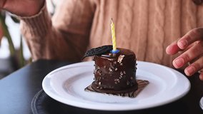 Focus on chocolate cake with a candle and hands of a woman, a birthday girl using a fork to break off, cutting a piece of delicious sweet dessert. Celebration. Life event. Pastry Cake In Restaurant. - Powered by Shutterstock - Get 15% off with code: PIKWIZARD15