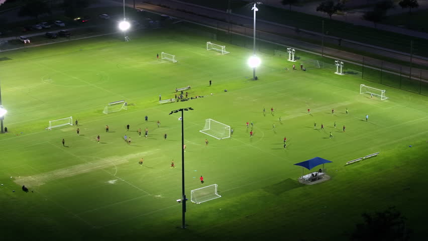 Illuminated public sports arena in North Port, Florida with people playing soccer game on grass football stadium at night. Outdoor activities concept Royalty-Free Stock Footage #3430544453
