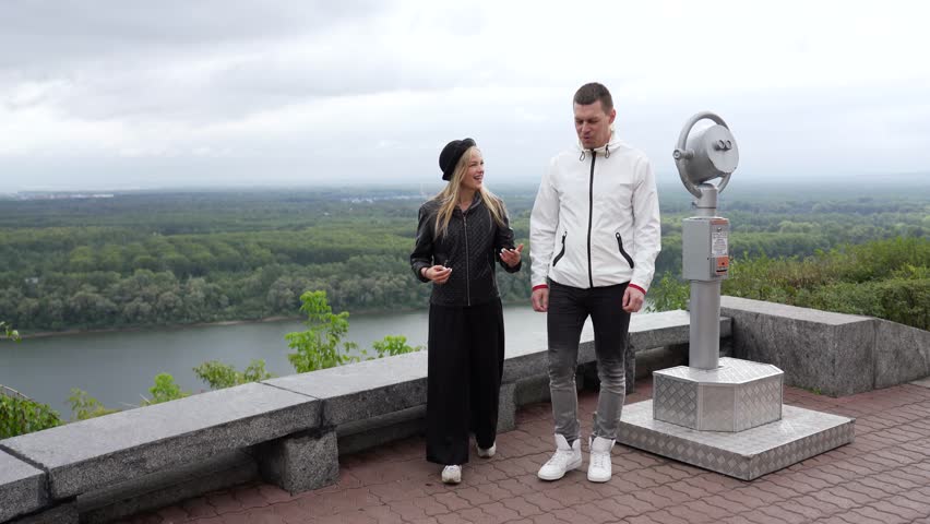 A girl and a man walk and talk against the background of a river.