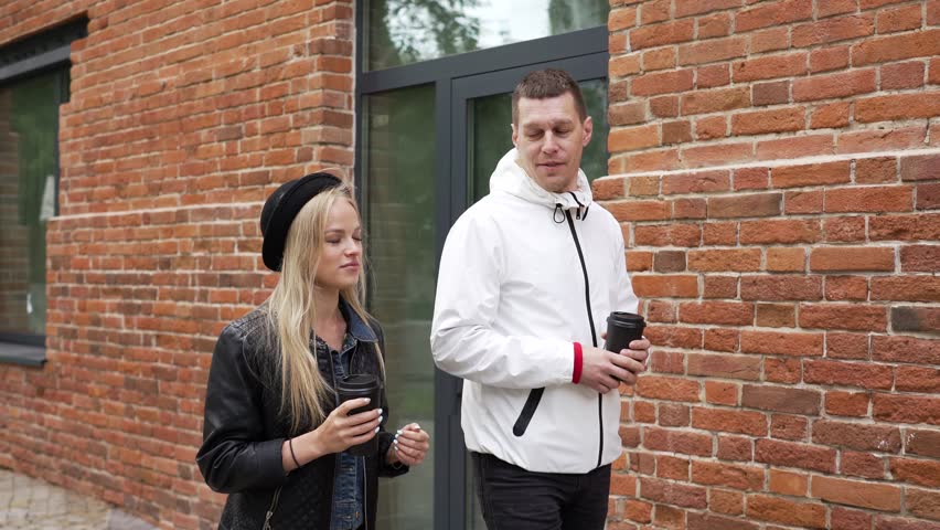 A man and a girl walk along a brick house and chat.