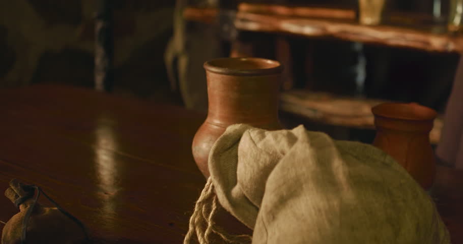 Medieval servant puts beer mug on wooden counter closeup. Barkeeper serves alcohol drinks in clay dishware in tavern. Drinking wine in old fashioned pub