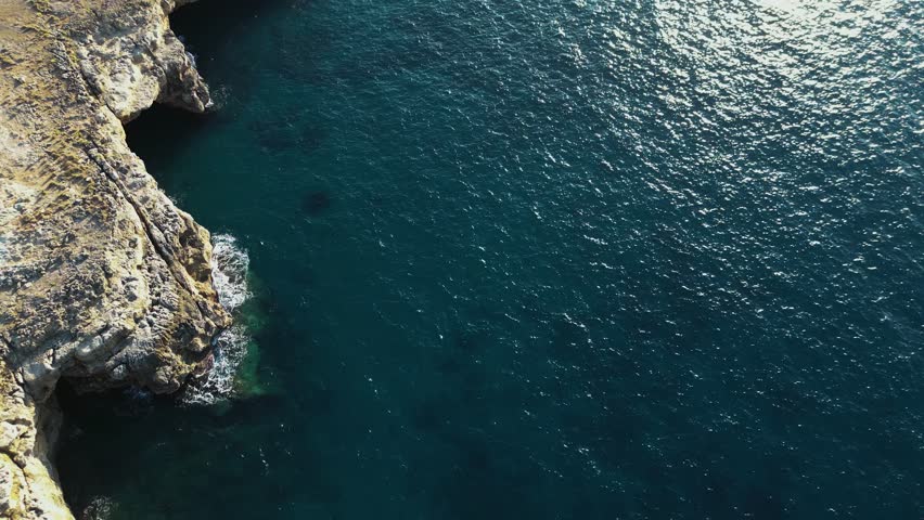 Drone video over inlet in the beautiful cristal transparent sea of Malia beach in Crete, Greece.  Summer travel in Greece at the rocky beach of Malia with an high cliff. Sunset over the sea water