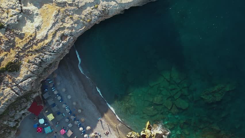 Drone video over inlet in the beautiful cristal transparent sea of Malia beach in Crete, Greece.  Summer travel in Greece at the rocky beach of Malia with an high cliff. Shore with sea waves.