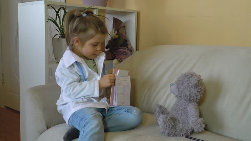 Caucasian girl in a white medical coat with a stethoscope treats a teddy bear, fills out a medical card, prescription, plays a hospital, plays a nurse, veterinarian Happy family, role-playing games Royalty-Free Stock Footage #3430684301