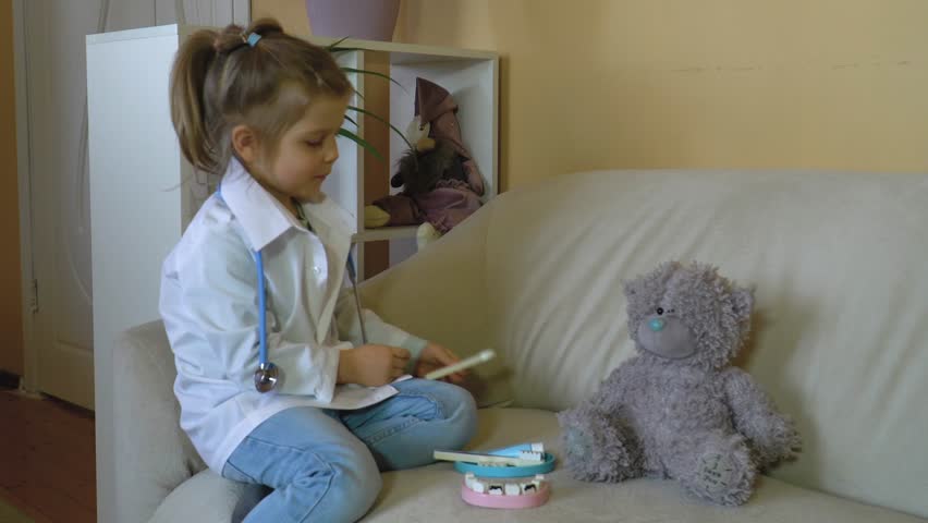 Caucasian girl in medical coat with stethoscope treats teddy bear, demonstrates brushing teeth, plays a hospital, plays a nurse, veterinarian Happy family, role-playing games, children's professions Royalty-Free Stock Footage #3430684869
