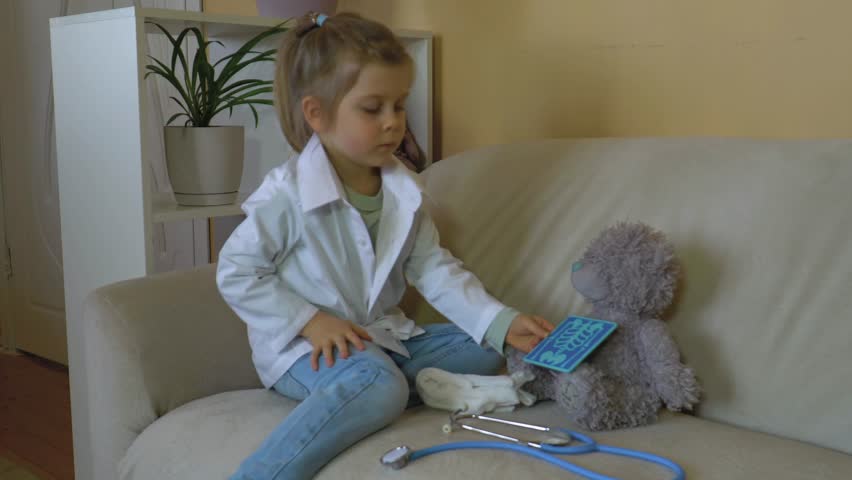 Caucasian girl in white medical coat with stethoscope treats teddy bear, looks X-ray, playing hospital, playing nurse, veterinarian Happy family, role-playing games, children's professions Royalty-Free Stock Footage #3430692275