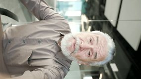 POV Vertical video. Senior gray haired businessman talking on video call using a phone in modern office. Elderly boss owner communicates looking at camera. Online chat with client or business partner - Powered by Shutterstock - Get 15% off with code: PIKWIZARD15
