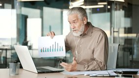Confident senior gray haired businessman giving online video call presentation using laptop sitting at workplace in business office. Elderly boss showing a chart, talking about company's development - Powered by Shutterstock - Get 15% off with code: PIKWIZARD15