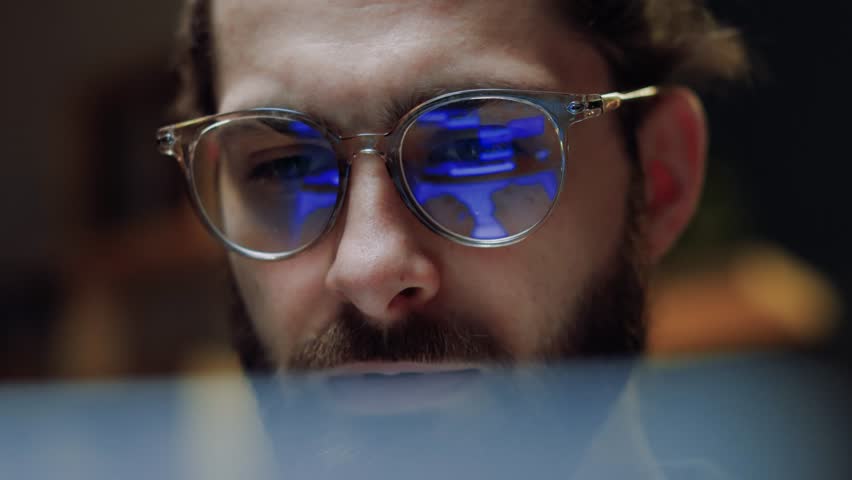 Close up eye reflection. Focused crypto trader analyst wearing eyeglasses working looking at computer screen reflecting in glasses analyzing online trading stock exchange market data charts.