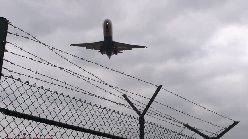 Airplane landing flies over barbed wire - slow motion