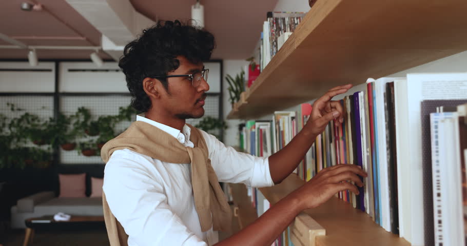 Serious focused Indian student guy visiting college or public library, read covers, choosing textbooks, preparing for higher institution admission or examinations. Getting new knowledge, intelligence Royalty-Free Stock Footage #3430795083