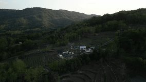 4k aerial video footage of house buildings in the mountain hills with empty fields and many lush trees around it during sunset.