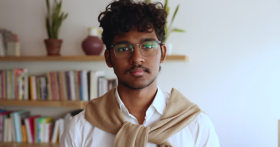 Head shot of Indian student guy in glasses posing on bookshelves background in campus library, smile look at camera. Excellent studies, getting higher education, generation Z person close up portrait Royalty-Free Stock Footage #3430809395