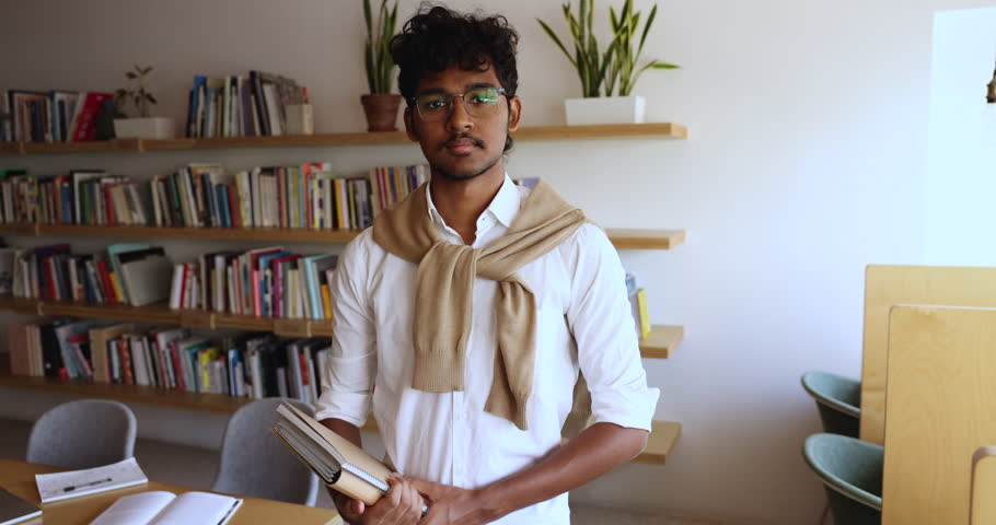 Portrait of smiling Indian male student holding educational materials, books, copybooks, pose alone in university library staring at camera. Excellent studies, new knowledge, gaining higher education Royalty-Free Stock Footage #3430830185