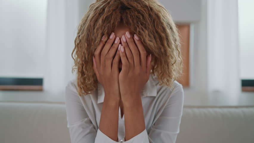 upset lady with blond curly hair sitting on the sofa in the living room. bad day at home slow motion