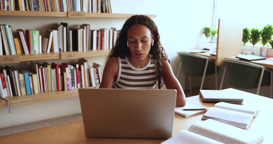 Pretty African girl studying on-line sit at desk using laptop, video calling to tutor or schoolmate, prepare for exams, take part in virtual meeting, gains news skills, share information. Education Royalty-Free Stock Footage #3430852091