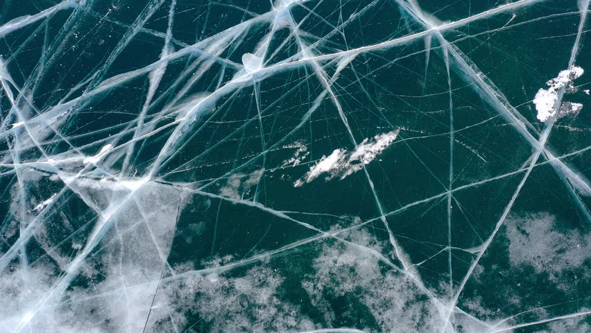 Aerial drone view frozen winter Lake Baikal. Blue transparent ice deep cracks top view. Natural cold background of ice. Winter abstract background. High quality 4k footage