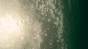 Vertical video, Underwater view of evening light of sun penetrates through drifting ice in current of water, Slow motion .The movement of ice down the river in sun rays at sunset