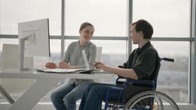 Colleagues, woman shows to man in wheelchair finance diagram document work together in office. Workers discuss analytics data process sit at desk. Usual life of people with physical disability. - Powered by Shutterstock - Get 15% off with code: PIKWIZARD15
