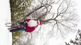 Vertical video footage of Santa Claus rides a bicycle in winter. A guy with a beard and wearing a Santa Claus hat rides through deep snow on a red bicycle. Slow Motion 2x