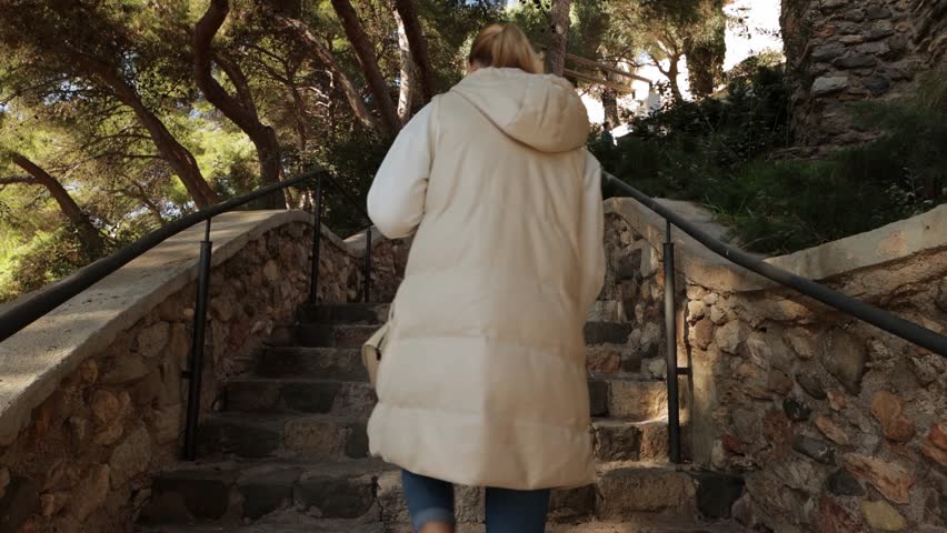 tourist girl in a light jacket climbs the stairs in a city park