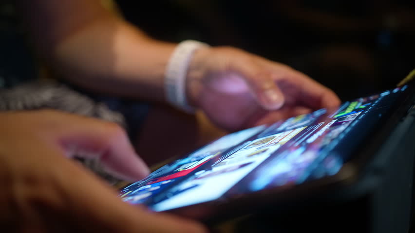 Young man scrolling content online, wireless internet. Closeup male hands searching on tablet screen, browsing videos or image content using WiFi at night. Close view modern tech device bright screen