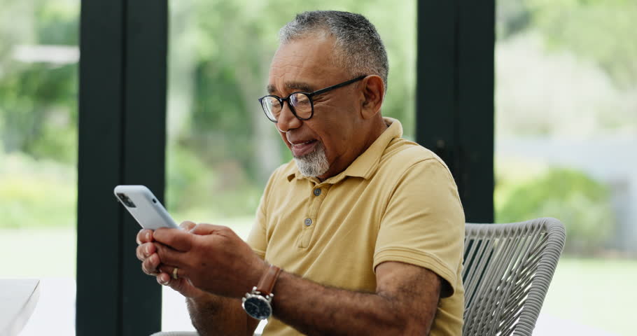 Phone, chat and happy senior man laughing in a house with comic, message or silly gif communication. Smartphone, app and elderly male person in a living room with funny, video or social media reel