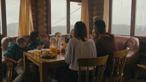 Multicultural family sit around table, eat, drink, talk and clink glasses. Friends gathered together in holiday home to rest. Tourists relax in wooden cottage during their vacation. Active leisure. - Powered by Shutterstock - Get 15% off with code: PIKWIZARD15