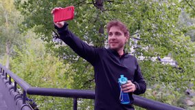 Young man making a video call on a smartphone holding a sports bottle with water outdoors.