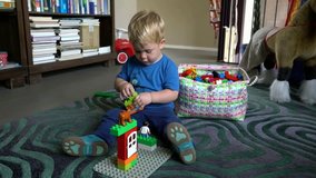 Two-year-old pretty blond boy playing with colorful lego on the carpet in the room
