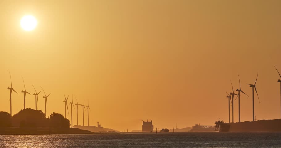 Timelapse of setting sun behind wind turbines and cargo ships traveling on the river, Rotterdam, Netherlands