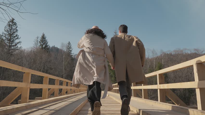 Spring, love and sunshine. A romantic walk where the two enjoy time together, illuminated by warm light. A young couple runs merrily on a wooden bridge. Happy having fun in nature