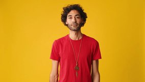 Attractive man with curly hair, dressed in red T-shirt, crossing his arms and looking at camera isolated on yellow background in studio