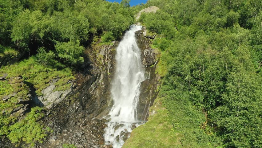 Large streams of waterfall among the branches of trees fall down in close-up. Smooth flight along.