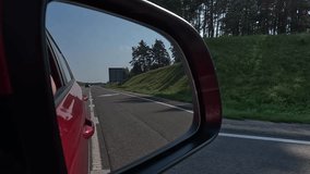 Video shooting in motion, view in the rear view side mirror of a auto, driving a red car along the road