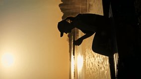 Vertical video Young woman drinks warm coffee at beautiful sunset, slow motion. Silhouette of girl in the setting sun sits on the parapet with coffee in hands and enjoys life. Cheerfulness, lifestyle