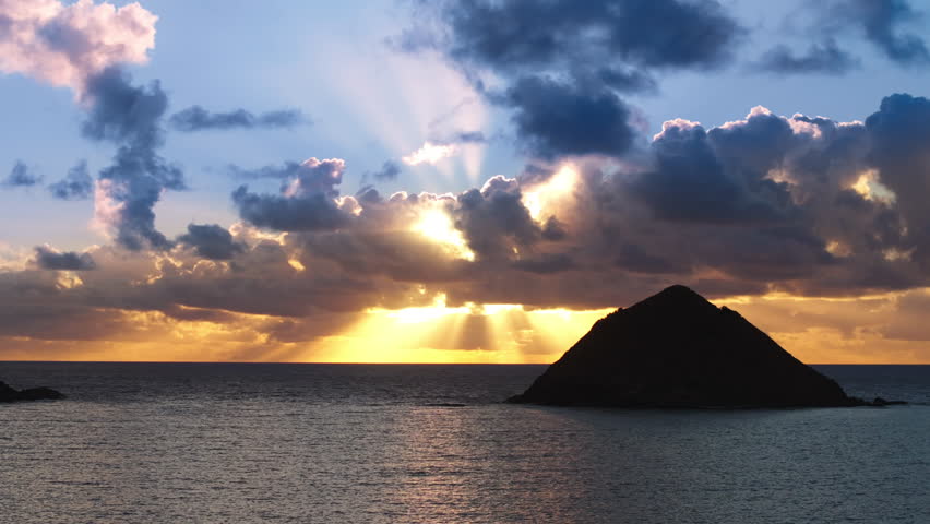 Breathtaking sunrise above Na Mokulua islands on windward coast of Oahu island. Bright golden sun beams shining through blue clouds above ocean. Dramatic nature on Hawaii islands. Oahu adventure trip Royalty-Free Stock Footage #3431681949
