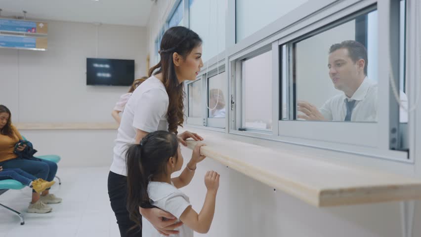 Asian family patient receive a medicine from pharmacy center in hospital. Attractive mom and daughter feeling happy and relax while waiting on line que to receive medicine in health medical clinic.