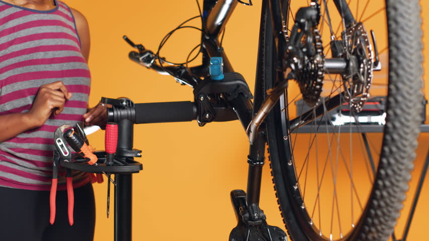 African american mechanic utilizing different tools to repair damaged bike handlebar grips, studio background. Employee using specialized gear to fix shifters and brake levers on bicycle, camera A Royalty-Free Stock Footage #3431732245