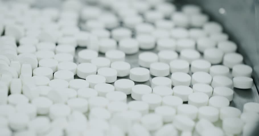 Process of production of pills, drugs. Factory equipment and machine conveyor. Industrial pharmaceutical concept. Factory equipment and machine. Closeup view of drugs move along conveyor belt.