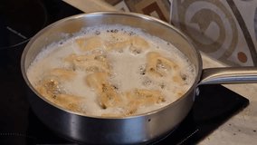 Frying traditional Polish sweet crispy biscuits called Faworki on the Pancake Day in deep hot oil in a steel frying pan