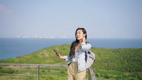 Asian woman relax and enjoy outdoor lifestyle travel nature trip at the sea on summer holiday vacation. Attractive girl using mobile phone taking selfie at tropical island mountain peak in sunny day.