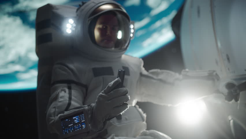 Young Astronaut Floating in Space in Zero Gravity. Spaceman Showing a Smartphone with Green Screen Mock Up Template. Male in a Spacesuit Posing for Camera, Smiling in Open Space Outside an Spacecraft Royalty-Free Stock Footage #3431929649
