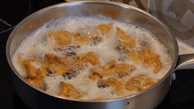 Frying traditional Polish sweet crispy biscuits called Faworki on the Pancake Day in deep hot oil in a steel frying pan