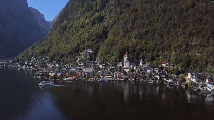 Flight around Hallstatt village over calm Hallstatter See at sunny summer morning, in Salzkammergut, Upper Austria.