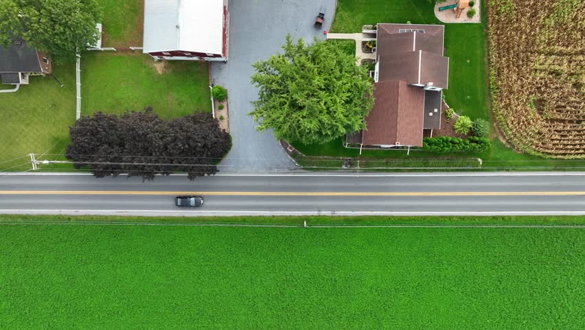 Road through rural American countryside in autumn. Homes and farms along country road. Aerial top down truck shot.