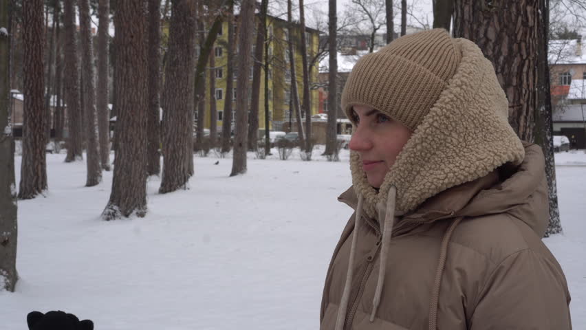 A girl on the street warms her hands by breathing on them. A walk in the winter park. In the open air. A woman wraps herself in a scarf so as not to freeze during the frost. Beige hat. 4k 